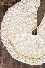 cream knitted Christmas tree skirt with a braided cable border flat laid on dark wood thumbnail