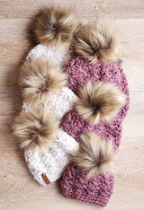handmade white and dusty rose textured crochet beanies with faux fur pom-poms on a wooden surface thumbnail