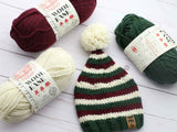 striped elf stocking cap with red, white, and green stripes and a white pom-pom, surrounded by matching skeins of yarn thumbnail
