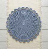dusty blue crocheted round placemat with gold surface stitch accent laid flat on a cream fringed table runner thumbnail