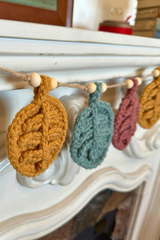 crocheted autumn leaf garland with wooden beads hanging across a mantelpiece thumbnail