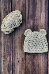 cream crocheted chunky bear beanie with ears and yarn on a wood background thumbnail