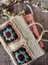 handmade crochet hearthside book sleeve holding a book with modern granny squares on a wooden surface thumbnail