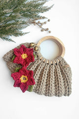 two crocheted red poinsettia appliqués with yellow centers and green leaves attached to a cream-colored textured crochet bag with wooden buttons thumbnail