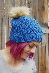 woman wearing a teal alpine stitch crochet beanie with a faux fur pom pom outdoors thumbnail