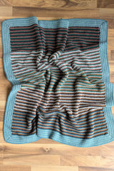 flat lay of a striped crochet baby blanket with a wide blue border on a wooden floor thumbnail