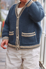 Close up of toddler wearing denim blue knit cardigan with cream ribbed trim ad pockets.  thumbnail