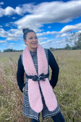 Woman standing in a field with a belted pink scarf thumbnail