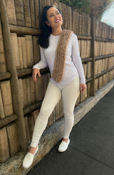 Woman in white stands against wall, wearing short brown scarf thumbnail