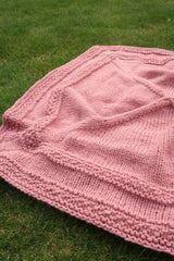 Pink knit blanket laid out on grass.  thumbnail