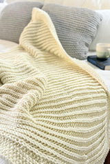 Close up of cream knit blanket, with books and mug in background.  thumbnail