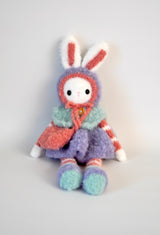Fuzzy crochet bunny with purple skirt, red & white striped arms & legs, and aqua vest. sitting up against white backdrop.  thumbnail