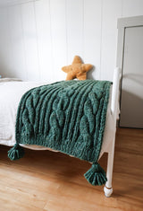 Green cabled throw on a white bed, with a golden star pillow in background.  thumbnail