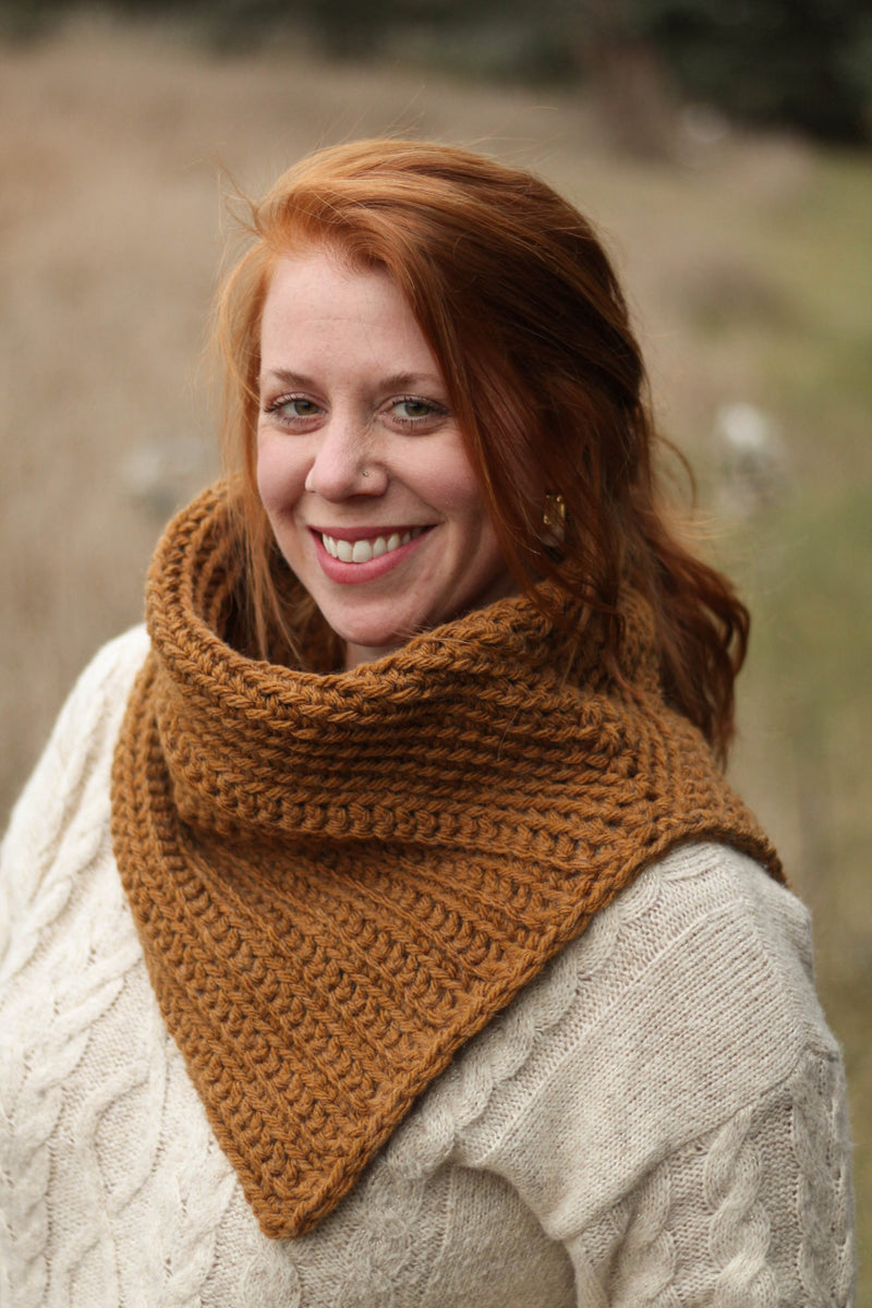 Model wears a golden orange crochet cowl over a cream top, while outdoors. 