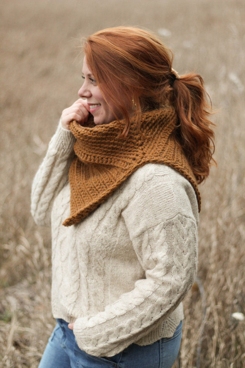 Side view of crochet cowl with slit to fit over shoulder, worn by model in cream sweater standing in a field. 