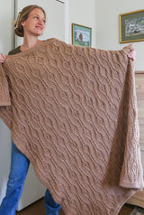 Woman holds tan crochet blanket, covering her from shoulder to ankle.  thumbnail