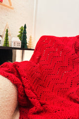 Red chevron ripple afghan on armchair with green pine tree decorations in background. thumbnail