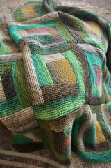 Knit log cabin blanket in shades of green, draped over footstool.  thumbnail