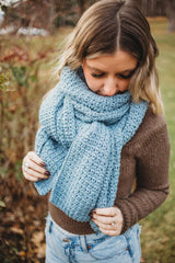 Woman wears pale blue crochet scarf wrapped & knotted around neck, standing in backyard.  thumbnail