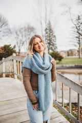 Woman wears pale blue crochet scarf, draped around shoulders, standing on wooden bridge.  thumbnail