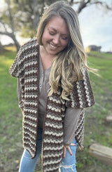 Woman leans toward camera, wearing tan shirt with short sleeve stripe crochet wrap over top.  thumbnail