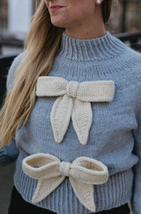Close up of pale blue sweater front with two cream bows.  thumbnail