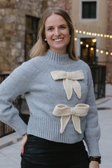 Woman wears pale blue knit sweater with two garter stitch bows in cream.  thumbnail