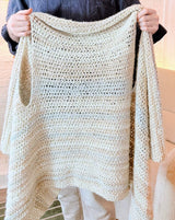 Man holds up crochet blanket vest by armholes.  thumbnail