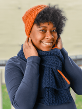Woman wears orange hat and navy blue crochet scarf, folded and pulled through loop.  thumbnail