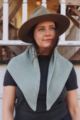 Woman in hat and grey t-shirt wears pale blue crochet shawl draped over shoulders.  thumbnail