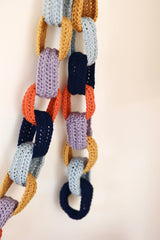 Detail shot of crochet chain garland, showing loops in dark navy, orange, lavender, mustard, and sky blue.  thumbnail