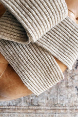 Squishy ribbed scarf in warm beige folded on leather footstool.  thumbnail