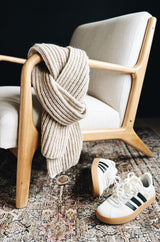 Beige ribbed scarf wrapped around arm of midcentury style chair, with sneakers on patterned rug.  thumbnail