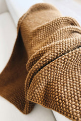 Close up of knit throw draped over the arm of a cream couch. The blanket is in a warm yellow brown and is knit in seed stitch for all over texture.  thumbnail