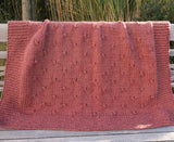 Full view of knit blanket with garter stitch border, draped over wooden bench.  thumbnail