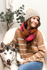 Woman wearing beige hat and orange pink crochet scarf sits in a cream chair with husky dog next to her.  thumbnail