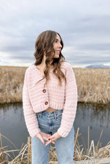 Woman wearing fuzzy pink cropped cardigan with jeans, standing on boardwalk in wetlands.  thumbnail