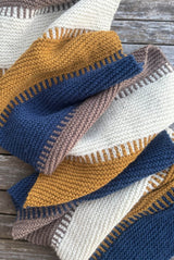 Garter stitch knit wrap in cream, taupe, blue, and golden yellow laying on wooden deck.  thumbnail