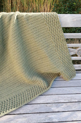 Warm olive green afghan photographed on wooden bench outdoors thumbnail