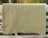 Folded olive green crochet blanket draped over back of wooden bench.  thumbnail