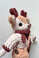 Side view of crochet deer showing ears and antlers, burgundy scarf, pink jacket, and peach bag.  thumbnail