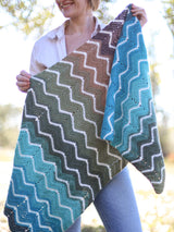 Woman holding wrap toward camera, showing chevron stripe pattern in multicolor yarn with small cream stripes.  thumbnail