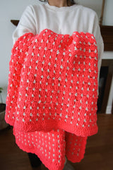 Neon pink crochet afghan with cream color accents held by woman in white sweatshirt.  thumbnail