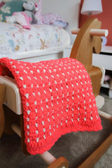 Crochet coral pink afghan draped over wooden rocking horse.  thumbnail