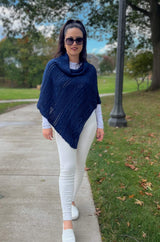Woman with dark hair and white jeans and sneakers wears a navy blue knit poncho in the park.  thumbnail