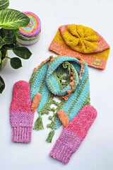 Multi-color crochet set of hat, scarf with bobble trim, and mittens, laid on white background. A plant peeks in frmo the left side.  thumbnail