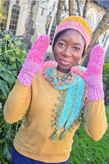 Woman in mustard yellow top holds hands in pink mittens up by face. She also wears a shirt crochet scarf and beanie that goes from pink to orange.  thumbnail