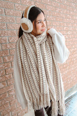 Woman in front of brick wall, wearing earmuffs and a crochet scarf in light neutral shades.  thumbnail