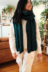 Woman in a cream outfit wears a dark teal cabled scarf.  thumbnail