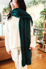 Woman in cream outfit wears green-teal cabled scarf tossed over one shoulder.  thumbnail